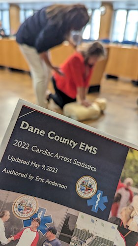Image of document that says Dane County EMS while in the background two people bend over a CPR dummy